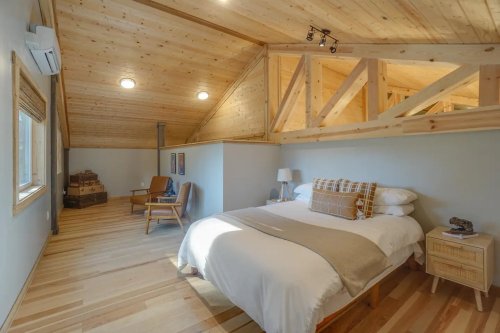 Cozy bedroom with a wooden ceiling, large bed, and minimalist decor, featuring natural light and warm tones.