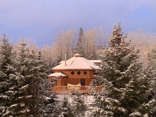 A cozy wooden cabin surrounded by snow-covered trees under a clear blue sky.