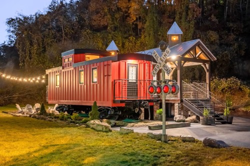 A red train caboose converted into a cozy home, surrounded by greenery and a decorative railroad crossing sign.