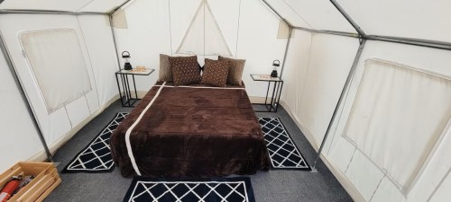 Cozy tent interior featuring a double bed with brown bedding, two side tables, and decorative rugs.