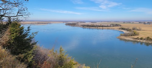 A serene river winding through a landscape of fields and trees under a clear blue sky.