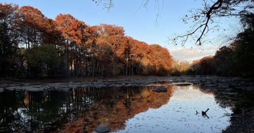 A serene river scene with autumn foliage reflecting on the water, surrounded by trees and rocks.