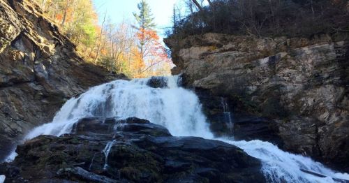 A cascading waterfall flows over rocky cliffs, surrounded by trees with autumn foliage.