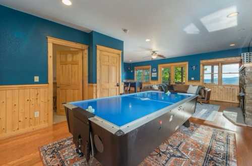 A game room featuring a blue pool table, wooden accents, and large windows with a view of the outdoors.