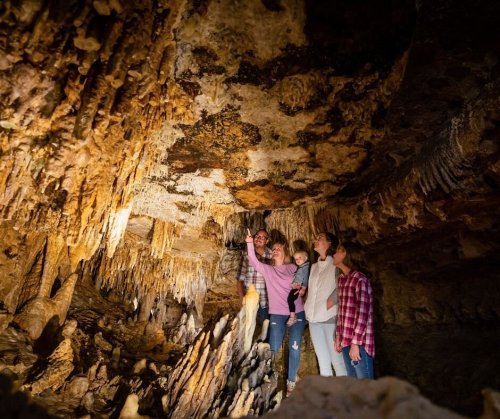 A group of five people exploring a cave, pointing at the rock formations and stalactites above them.