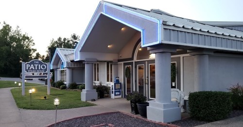 Exterior view of The Patio Steakhouse, featuring blue neon lights and a welcoming entrance surrounded by greenery.