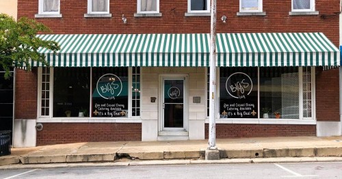 A brick building with green and white striped awnings, featuring large windows displaying a casual dining establishment.