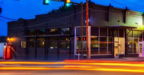 A dimly lit building at dusk with colorful lights, traffic streaks, and a vintage phone booth nearby.