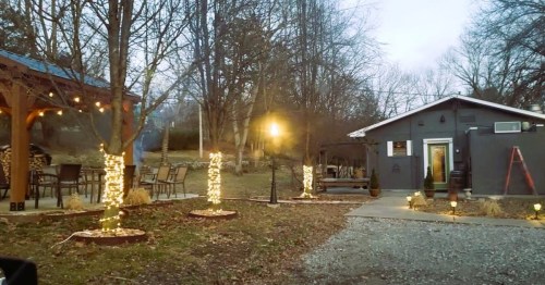 A cozy outdoor space with string lights, a small building, and trees, creating a warm evening atmosphere.