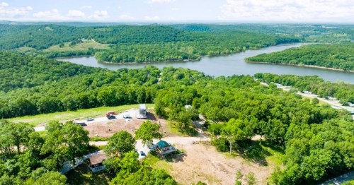 Aerial view of a lush green landscape with a river, trees, and a small building near a clearing.