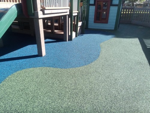 Colorful playground surface with blue and green rubber flooring, featuring a play structure in the background.
