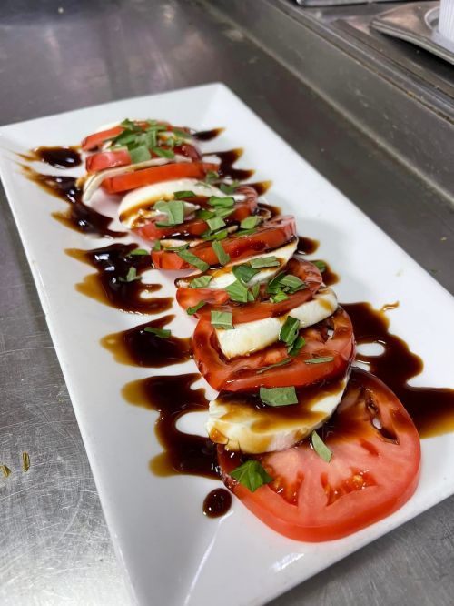 A plate of sliced tomatoes and mozzarella drizzled with balsamic glaze, garnished with fresh basil.