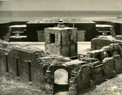 Black and white photo of a historic fort with crumbling walls, surrounded by water and a clear sky.