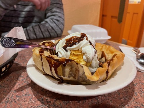A dessert bowl with a crispy shell filled with ice cream, whipped cream, and chocolate sauce.
