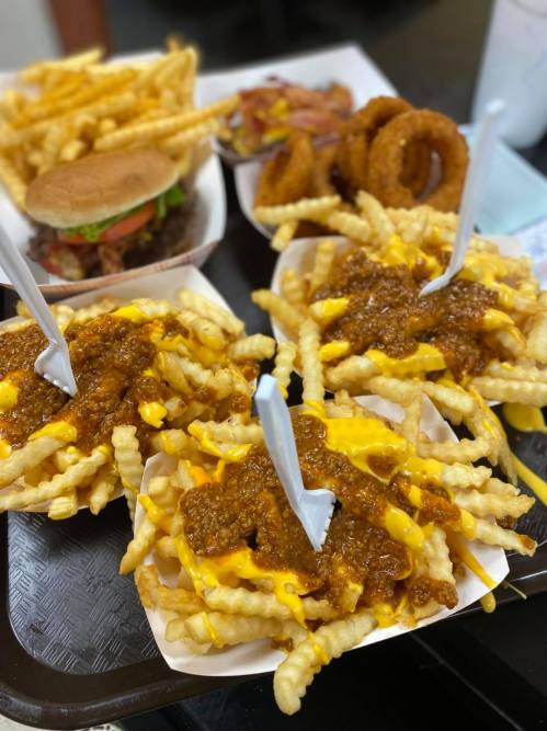 A tray of food featuring loaded fries with cheese and chili, a burger, onion rings, and a side of fries.