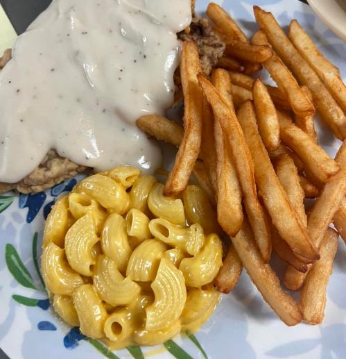 A plate with fried chicken smothered in gravy, macaroni and cheese, and crispy French fries.