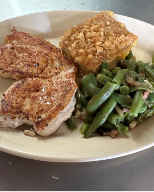 A plate with grilled chicken, green beans, and a slice of cornbread topped with a crunchy topping.