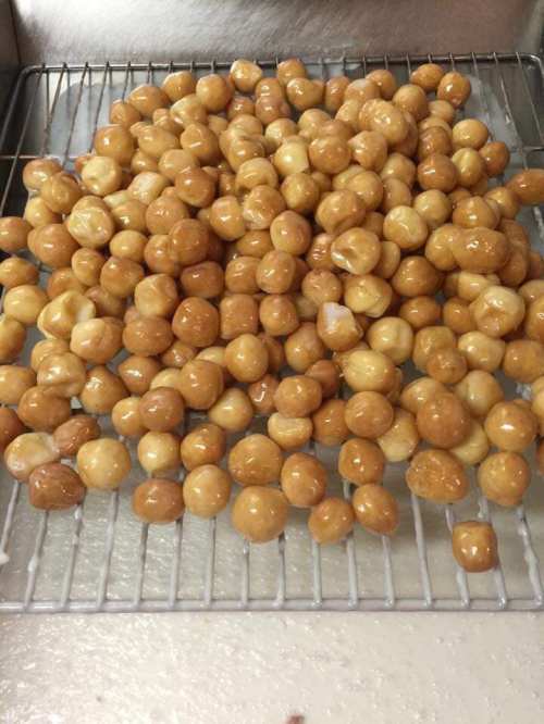 A close-up of a wire rack filled with small, round, golden-brown dough balls, glistening with a sugary glaze.