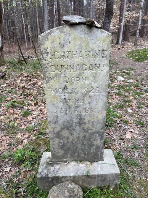 A weathered gravestone in a forest, inscribed with "Catherine Dunnagan, Born May 7, 1828, Died Jan 6, 1874."
