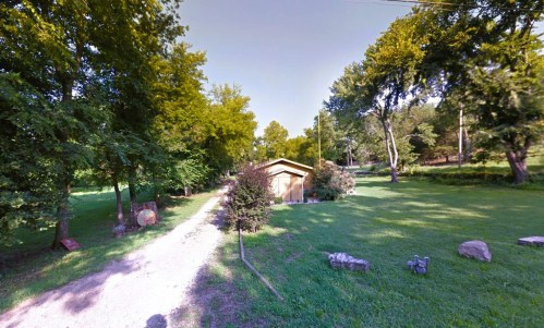 A gravel path leads to a small wooden building surrounded by trees and grassy areas.