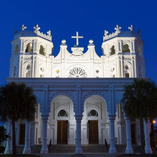 A beautifully lit church at dusk, featuring ornate architecture and a prominent cross atop its steeple.