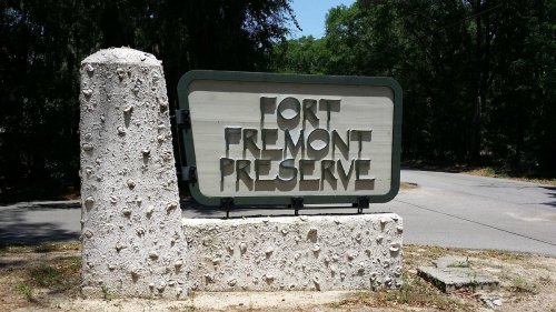 Sign for Fort Fremont Preserve, featuring bold lettering on a stone structure, surrounded by greenery.