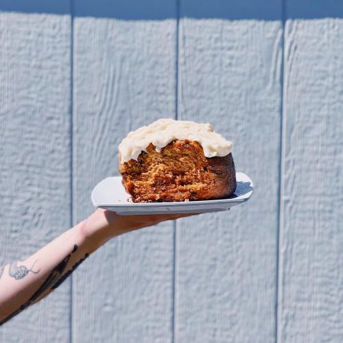 A person holding a slice of cake on a plate against a textured blue background.
