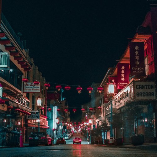 A quiet street in Chinatown, illuminated by red lanterns, with buildings lining the sides and a calm atmosphere.