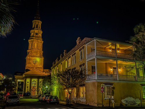 Historic building with a tall clock tower, illuminated at night, alongside a charming two-story structure.