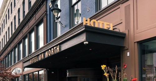 Exterior of Hotel on North, featuring a sign and colorful flowers in front of a historic building.