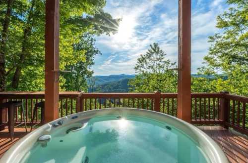 A hot tub on a wooden deck overlooking a scenic view of lush green mountains and a bright sky.