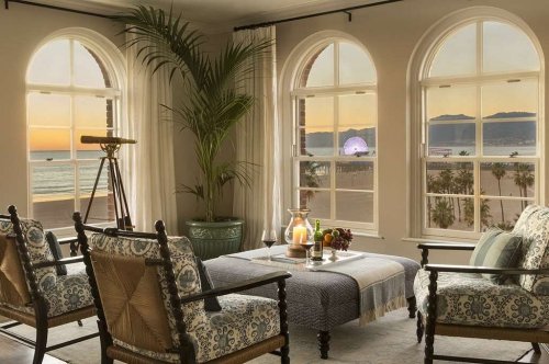 Cozy living room with ocean view, featuring elegant chairs, a telescope, and sunset lighting through arched windows.