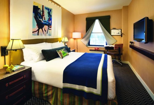 Cozy hotel room with a large bed, colorful decor, a window with drapes, and a TV on the wall.