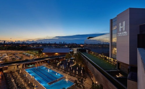 A modern building with a pool at dusk, featuring city skyline in the background and illuminated signage.