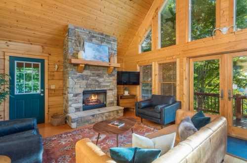 Cozy wooden cabin interior with a stone fireplace, large windows, and comfortable seating.