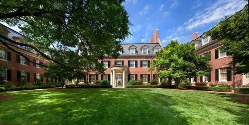 A large brick building surrounded by lush green lawns and trees under a blue sky.