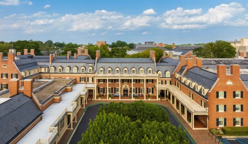 Aerial view of a historic brick building with a courtyard and green trees, under a blue sky with scattered clouds.