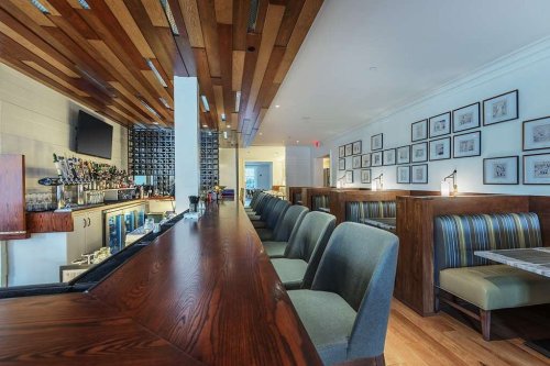 A modern restaurant interior featuring a wooden bar, high-backed seating, and framed artwork on the walls.