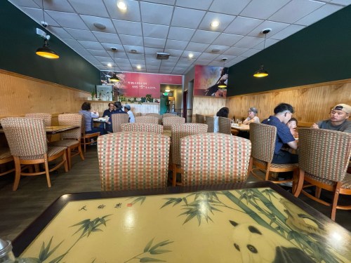 A cozy restaurant interior with wooden walls, empty tables, and diners enjoying meals in the background.