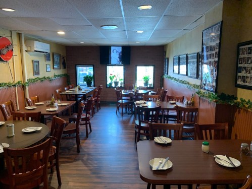 Cozy restaurant interior with wooden tables, chairs, and plants, featuring framed photos on the walls.