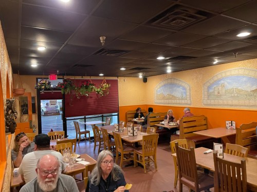 A cozy restaurant interior with wooden tables, patrons dining, and colorful wall decor.