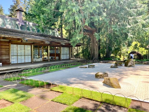 A serene garden with a wooden building, stone features, and lush greenery, creating a peaceful outdoor space.