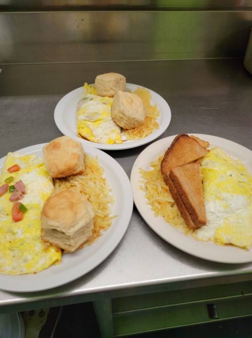 Two plates of breakfast featuring omelets, hash browns, biscuits, and toast.
