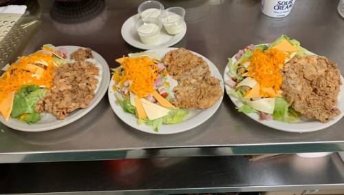 Three plates of food featuring fried chicken, salads with cheese, and dressings on a countertop.