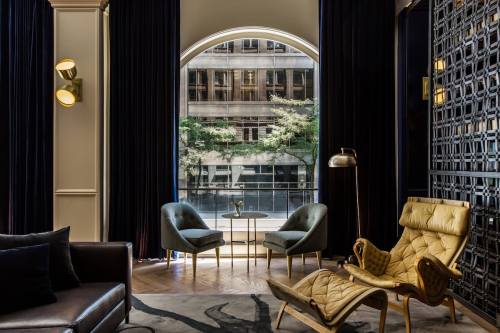 A stylish lounge with a golden chair, two gray chairs, and large windows overlooking a cityscape.
