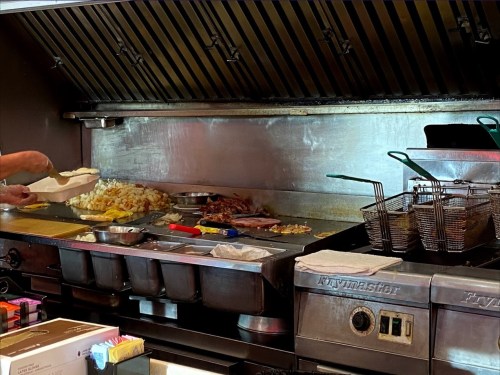 A busy kitchen grill with various cooked foods, frying baskets, and a chef preparing a dish.