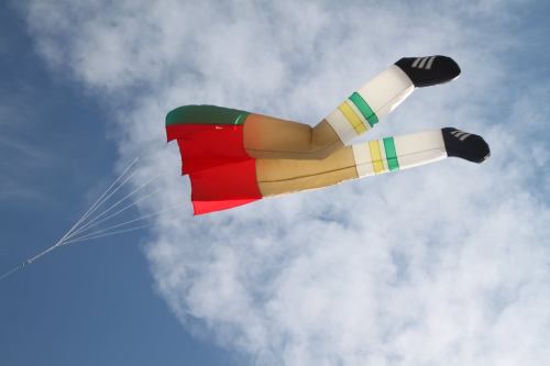A colorful kite shaped like a pair of legs with striped socks flying against a blue sky with clouds.