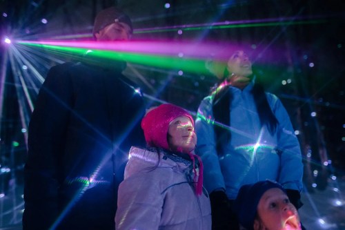 A family stands in awe under colorful laser lights, with beams illuminating their faces in a festive atmosphere.