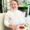 A smiling woman in a white sweater sits at a table with a plate of cookies and a cup of tea.
