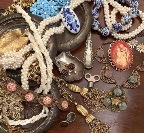 A collection of vintage jewelry and accessories, including pearls, beads, and ornate brooches, arranged on a wooden surface.